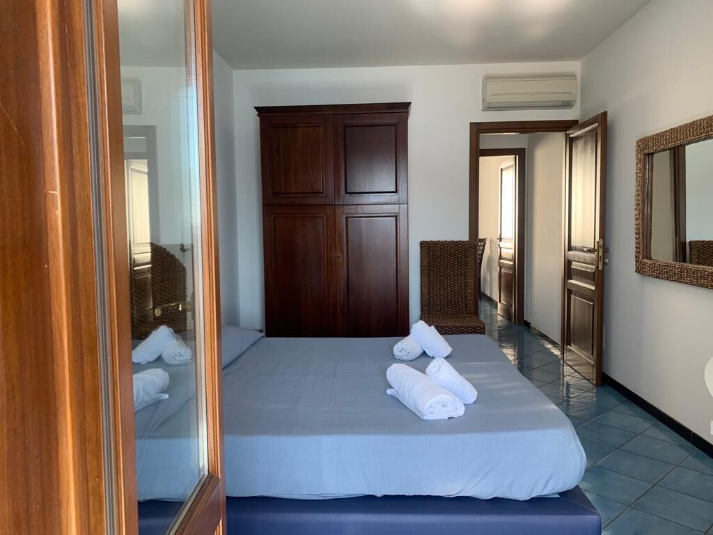 A hotel room with a bed, a wardrobe, a mirror, and a wicker chair.