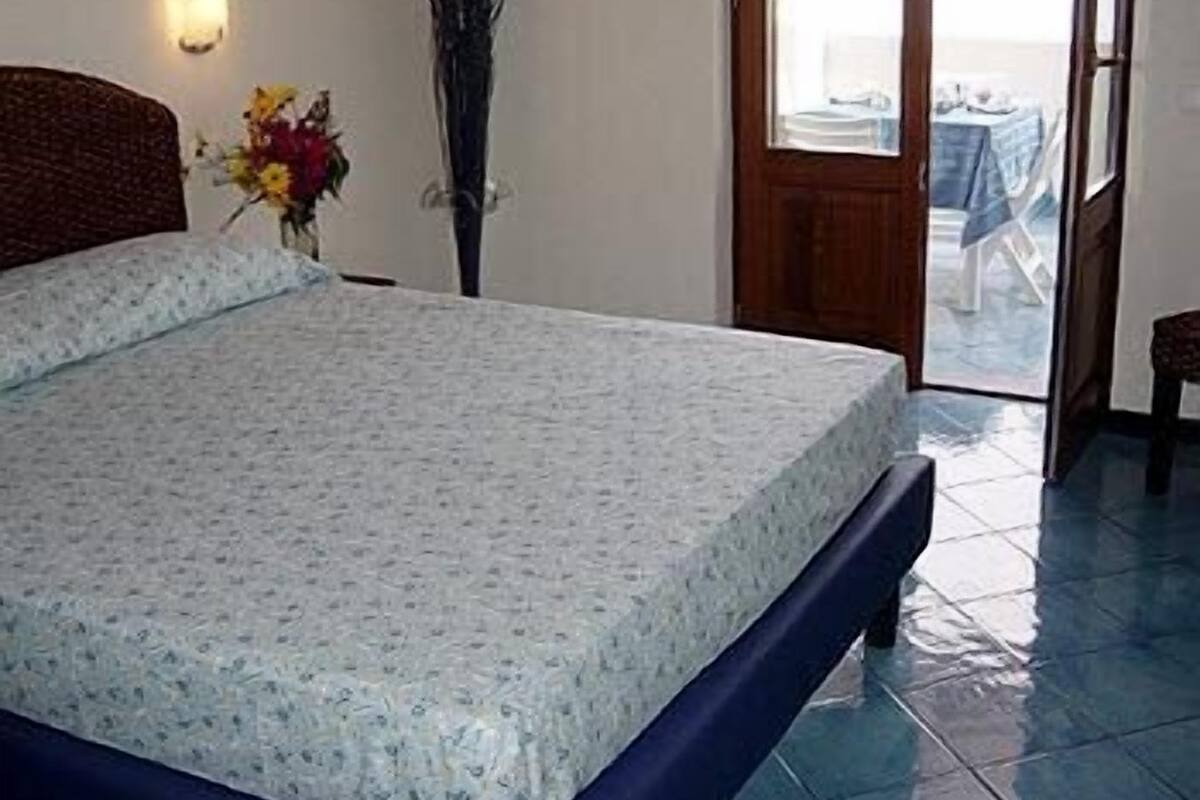 A bedroom with a bed, a vase with flowers, and a view of the outside.