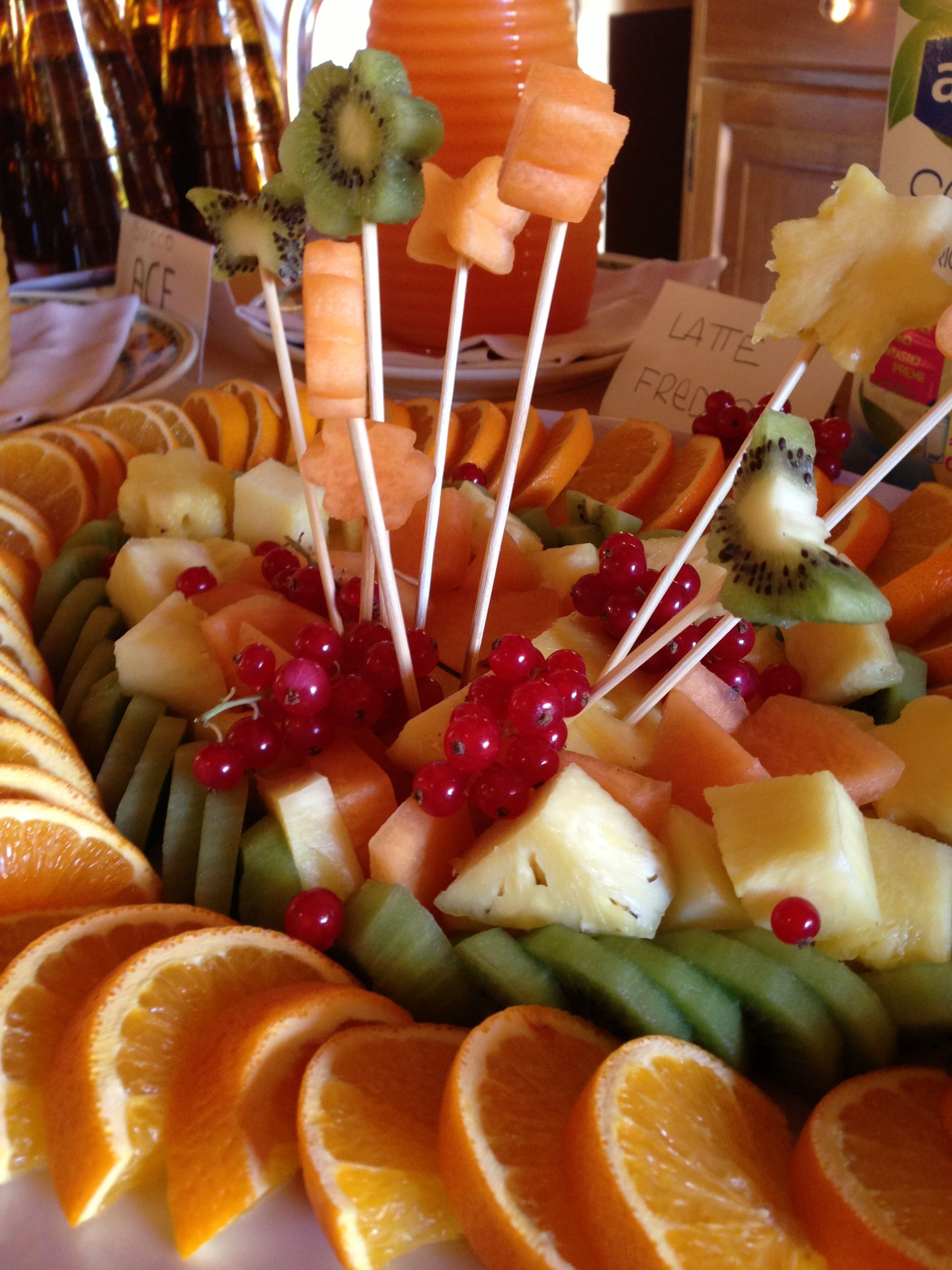 A fruit platter with various fruits and vegetables, including kiwi, cantaloupe, and oranges, arranged on a plate.
