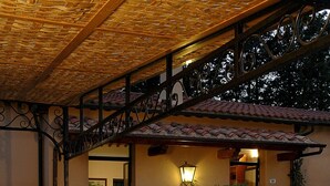 An outdoor dining area with round tables set for two, featuring metal chairs and a pergola overhead. - Fattoria Casabianca (Murlo)