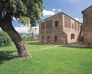 A stone building with a grassy courtyard, a tree, and a clear sky.
