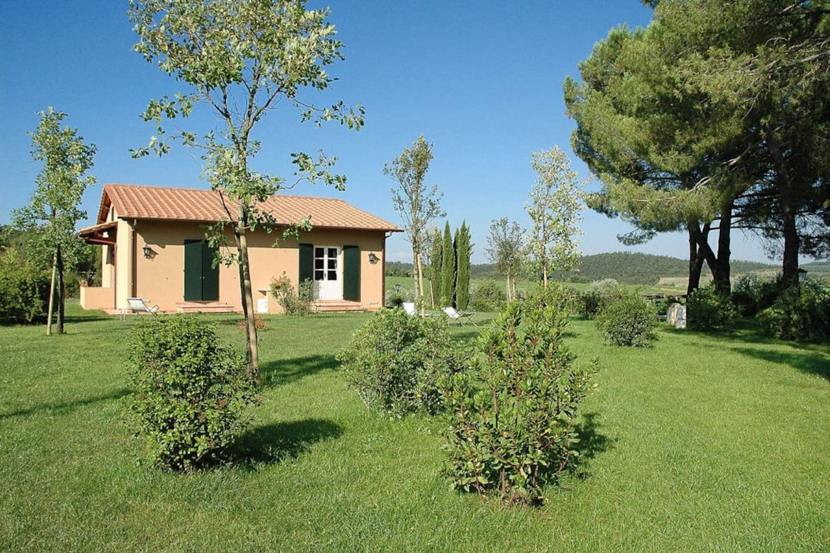 A single-story house with a tiled roof, surrounded by a well-maintained lawn and several trees.
