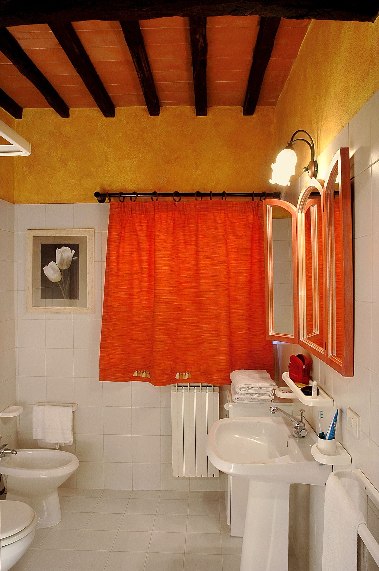 Une salle de bain avec deux lavabos, des toilettes, un bidet, un rideau de douche, un porte-serviettes, un miroir et un tableau encadré au mur.