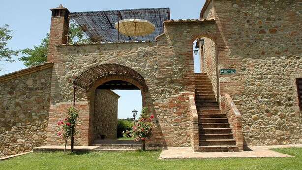 A stone building with an arched entrance, a staircase leading to a second level, and a sign indicating apartments 101-102. - Fattoria Casabianca (Murlo)