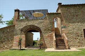 A stone building with an arched entrance, a staircase leading to a second level, and a sign indicating apartments 101-102. - Fattoria Casabianca (Murlo)