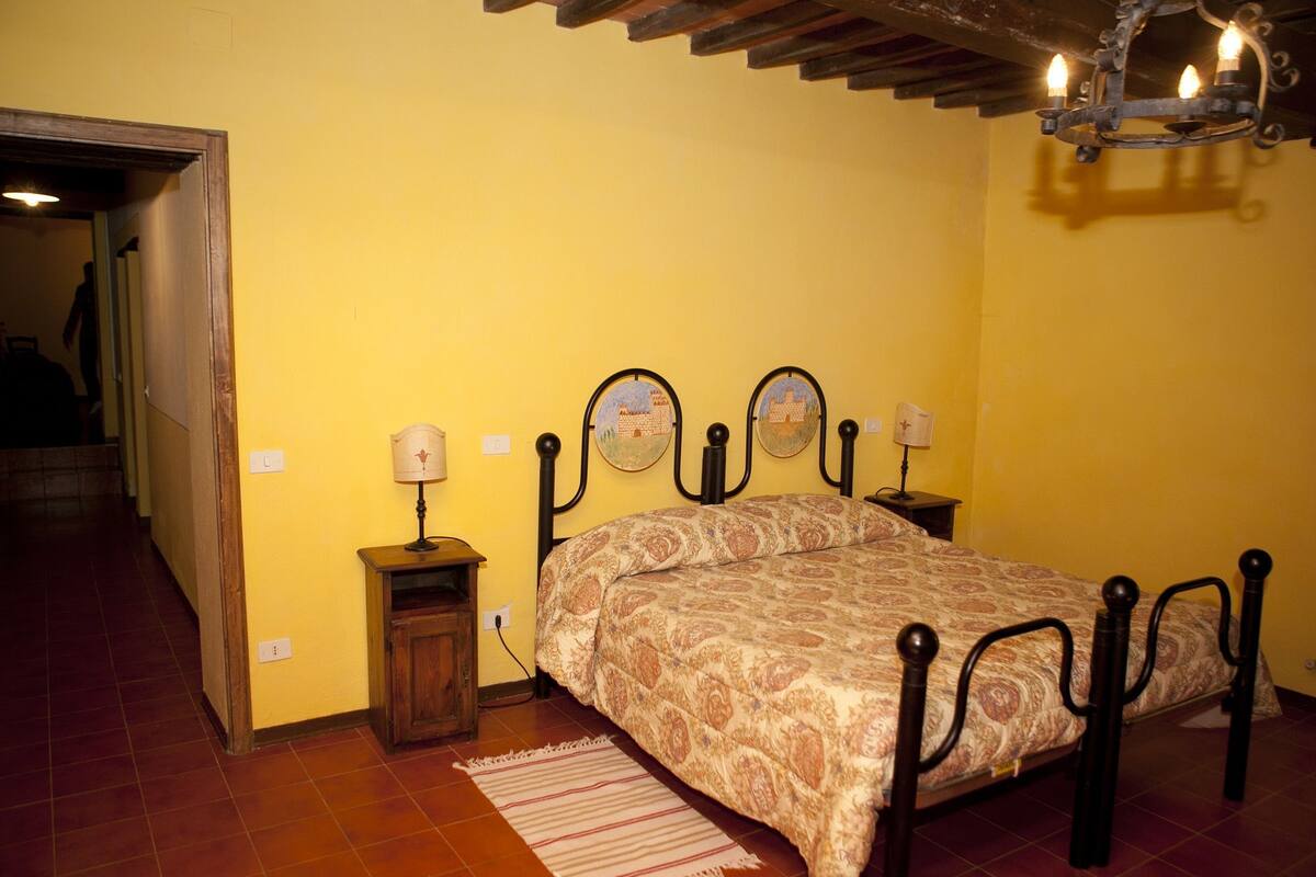 A bedroom with a bed, bedside lamps, a nightstand, a rug, and a wooden ceiling.