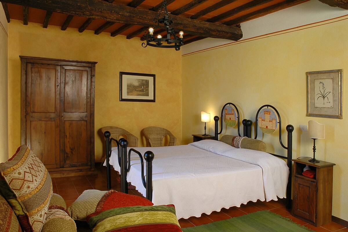 A bedroom with a wooden bed, two chairs, a nightstand, and a chandelier.