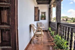 Een balkon met rieten stoelen, bloempotten en uitzicht op een heuvel.