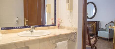 A bathroom with a marble sink, a towel rack, a mirror, a hairdryer, and a wooden chair.