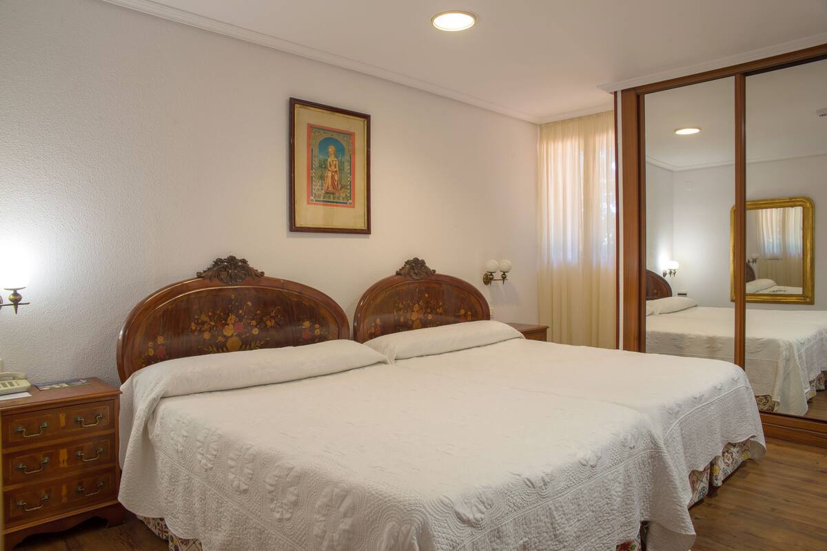Una cama doble con cabecera de madera, una mesita de noche con lámpara, y un cuadro enmarcado en la pared.