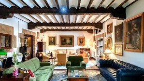 Un salón amplio con techos altos, vigas de madera y diversas opciones de asientos, incluyendo un sofá verde, un sofá azul y un sillón verde.