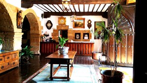 Un interior rústico con una mesa de madera, plantas en macetas y un amplio arco.