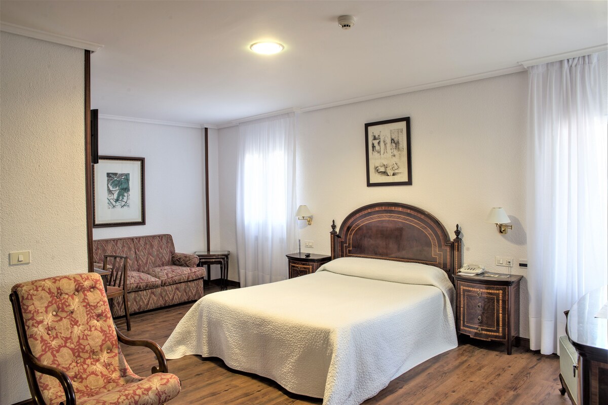 Ein Hotelzimmer mit einem großen Bett, einem Sessel, einer Couch, einem Nachttisch und einer Lampe.