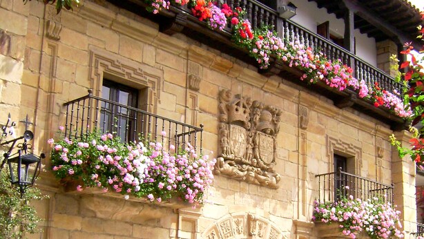 Fachada de hotel con revestimiento de piedra, un escudo sobre la entrada y macetas con flores en los balcones.