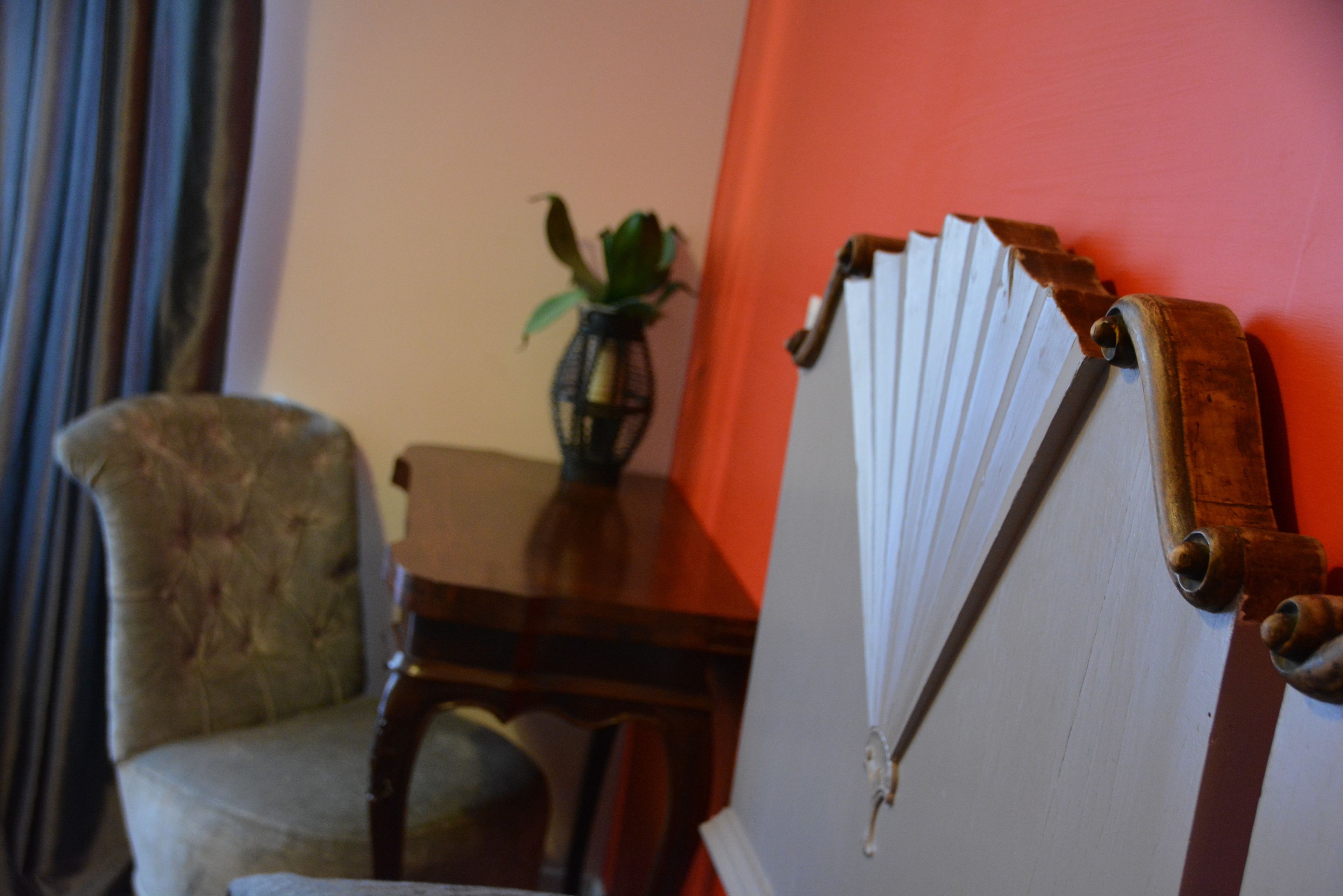 A room with a wooden chair, a small table with a plant, and a white fan against a red wall.