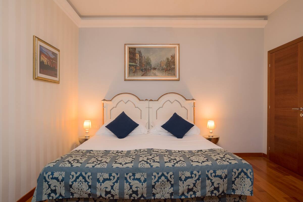 Ein ordentlich bezogenes Bett mit einer gemusterten Tagesdecke, zwei Kissen und zwei Nachttischlampen.