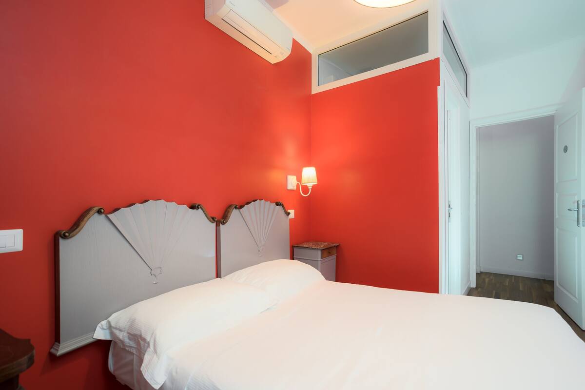 Ein Zimmer mit einem Bett, einem Nachttisch, einer Wandleuchte und einem Deckenventilator.
