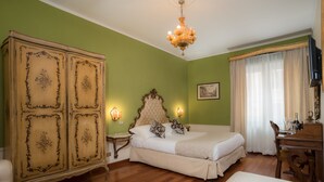 Ein Schlafzimmer mit großem Holzschrank, Bett mit weißer Bettwäsche, einer Chandelierleuchtre und einem Schreibtisch mit Stuhl.