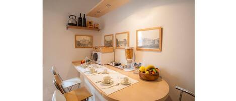 Una cocina con encimera de madera, un lavamanos y una silla. Hay cuadros en la pared y un cuenco con fruta en la encimera.