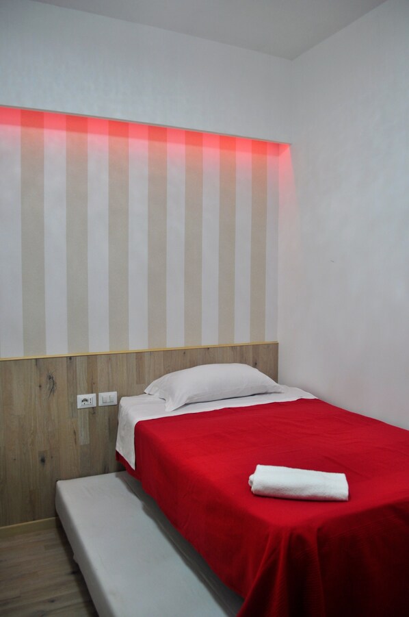 A single bed with a red bedspread and white pillows, a wooden headboard, and a red-striped wall. - Angela Roma (Rome)
