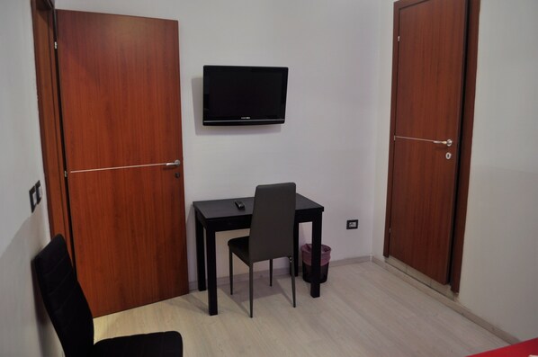 A small room with a wooden desk, a chair, a television mounted on the wall, and two wooden doors. - Angela Roma (Rome)
