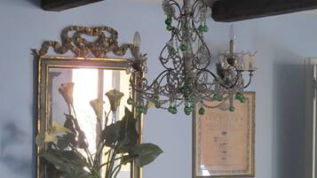 Un comedor con una mesa y sillas de madera, una lámpara de araña, un espejo con marco decorativo y una placa en la pared.