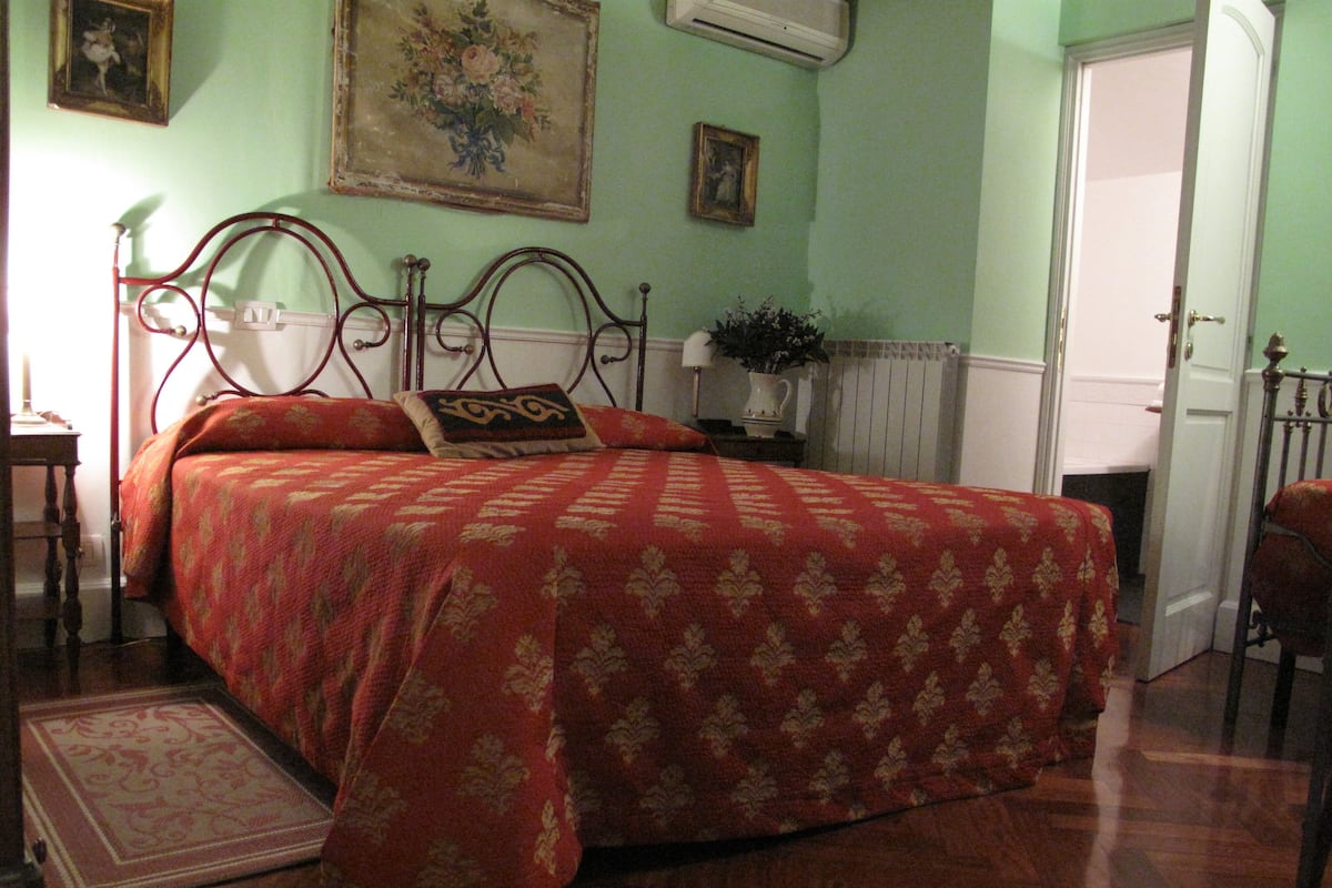 Un dormitori amb un llit amb cortines, una tauleta de nit amb una làmpada, un radiador i una porta.
