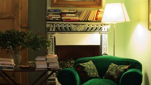Een kamer met een groene fauteuil, een houten kast, een open haard en een spiegel aan de muur.