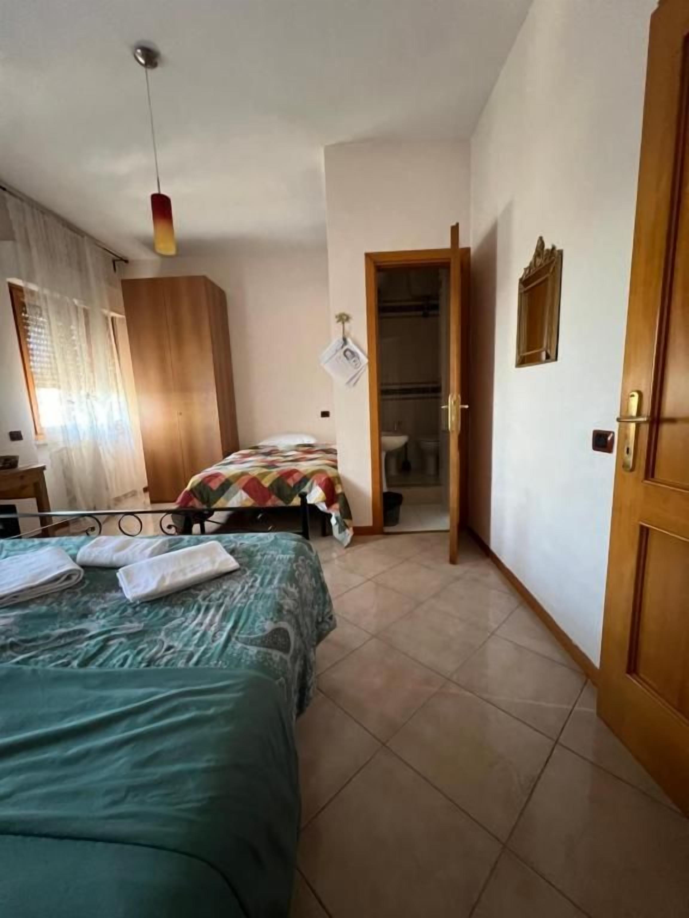 A bedroom with a bed, a wooden wardrobe, a door, and a hanging light fixture.