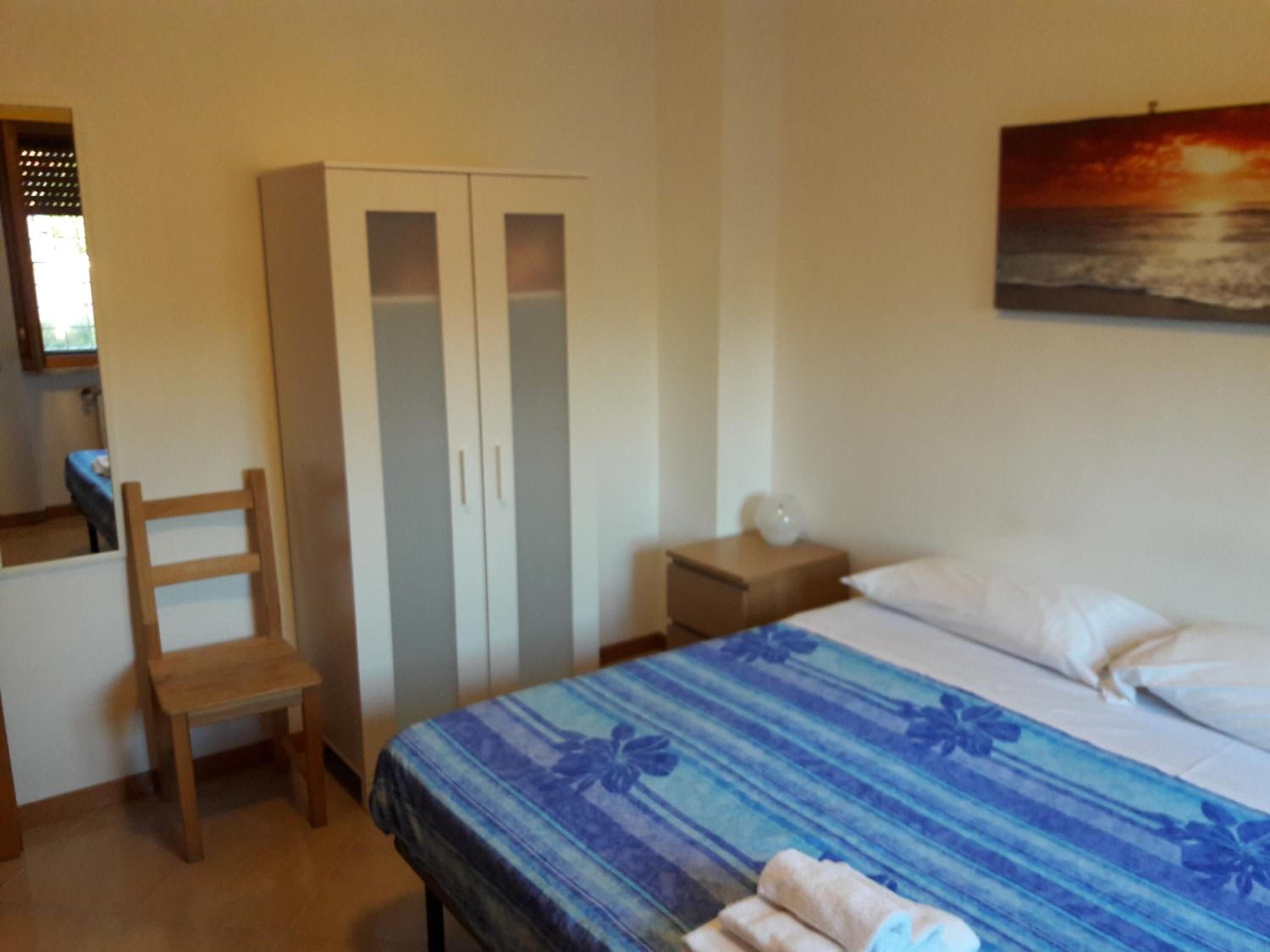 Une chambre à coucher comprenant un lit, une armoire, une table de chevet, une chaise et un tableau représentant un coucher de soleil.