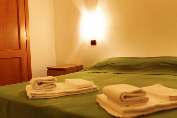 Una habitación de hotel con una colcha verde, una puerta de madera y una mesita de noche con una lámpara.