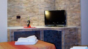 A hotel room with a stone-patterned wall, a flat-screen TV mounted above a wooden bench, and two beds with red and orange bedding. - Nuova Fiera Aparthouse (Rome)