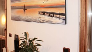 A dining area with a wooden table and chairs, a potted plant, and a wall-mounted painting of a sunset over water. - Nuova Fiera Aparthouse (Rome)