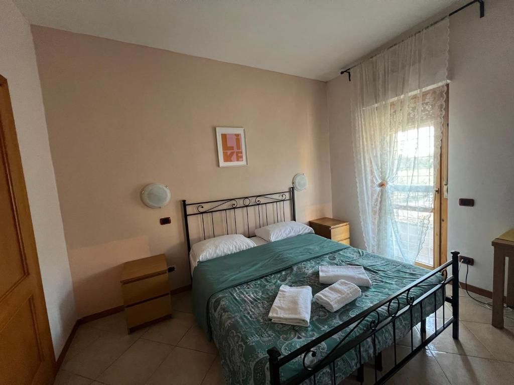 Un dormitorio con cama, mesitas de noche, una ventana con cortinas y una lámpara fijada a la pared.