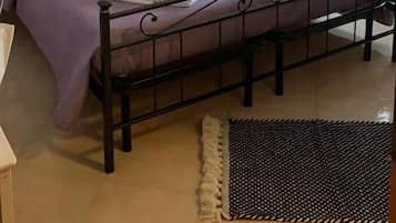 En säng för en person med en metallram, ett sängbord och ett fönster med gardiner.