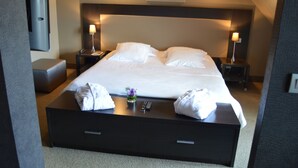 A hotel room with a large bed, two bedside tables with lamps, a small vase with a flower, and a painting on the wall. - Hôtel les Rives (Guebwiller)