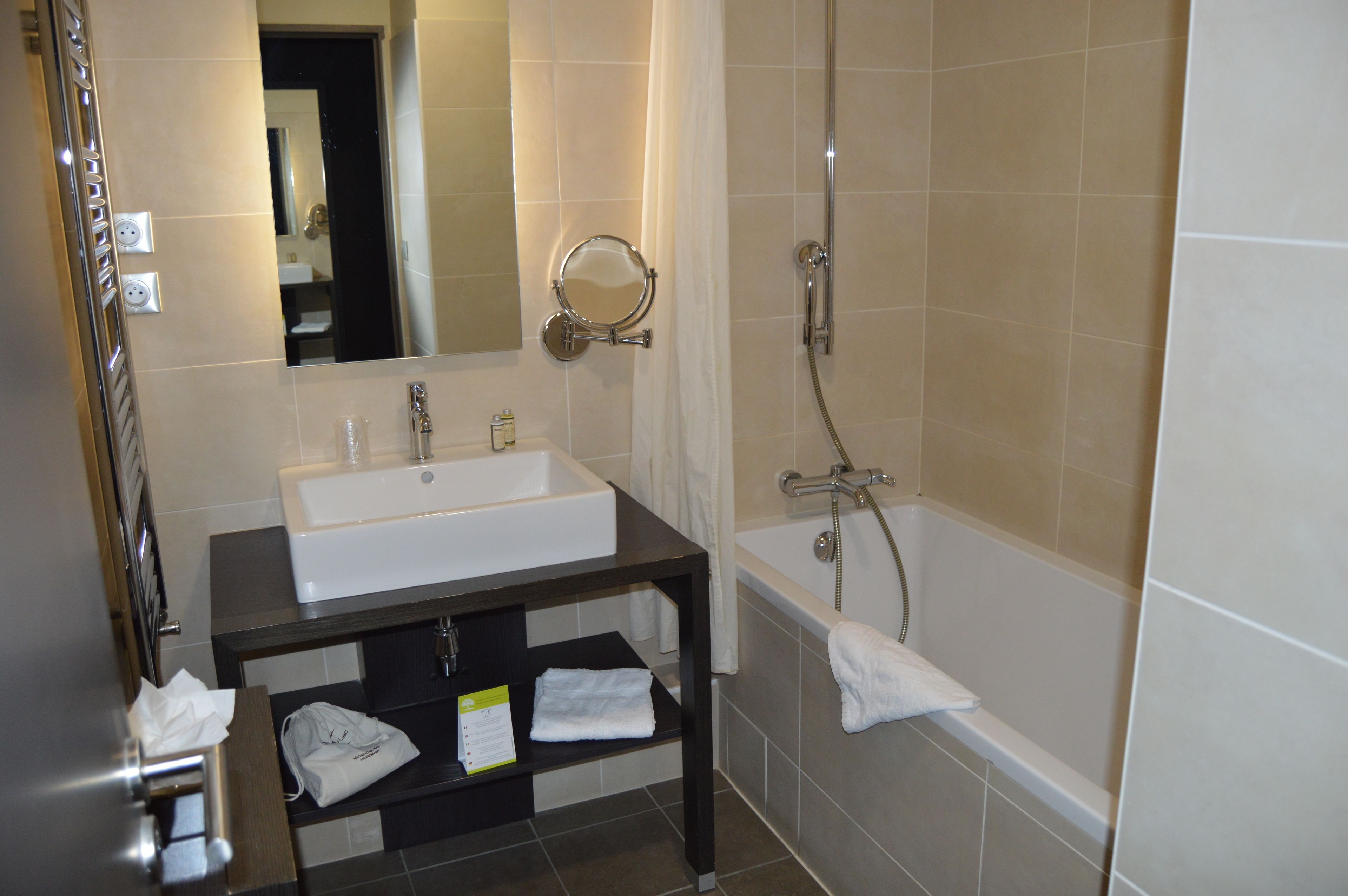 A bathroom with a sink, mirror, shower, and a towel rack.