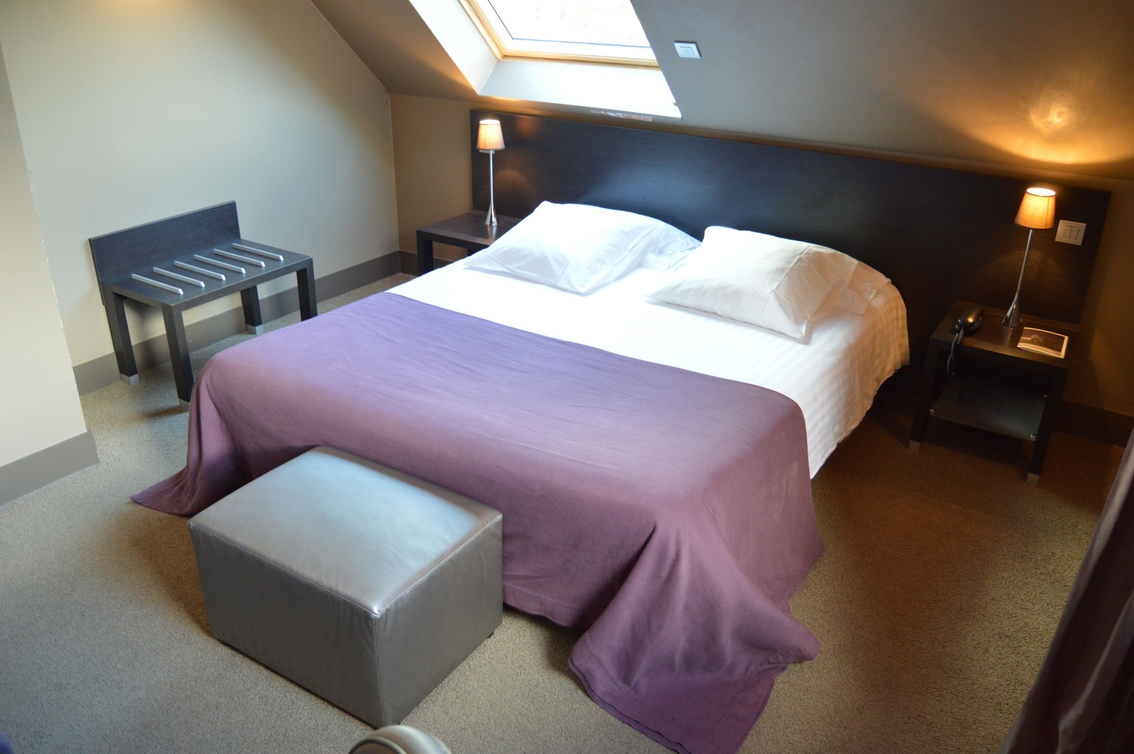 A bedroom with a bed, a bench, a bedside table, a lamp, and a telephone.