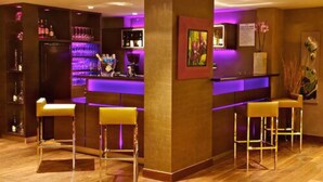 A bar area with a counter, bar stools, and a shelf with bottles. - Hôtel les Rives (Guebwiller)