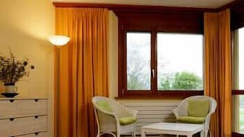 A hotel room with a bed, two chairs, a dresser, and a window with curtains.