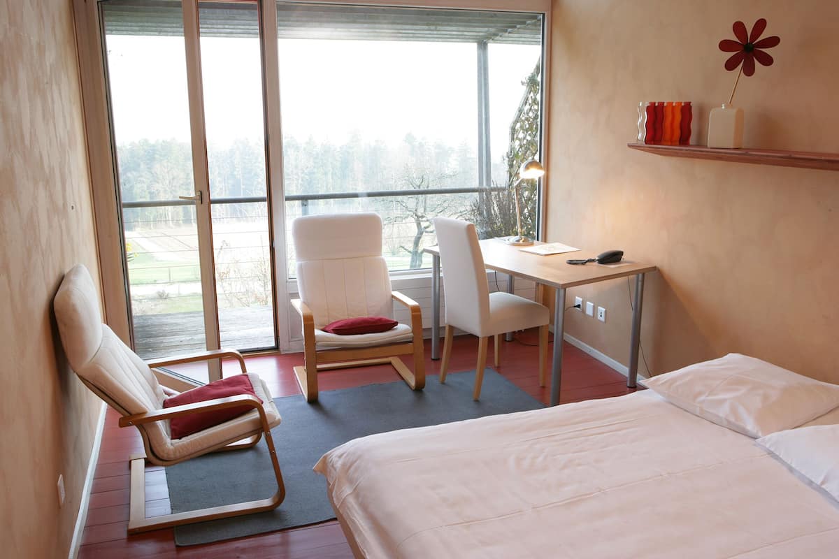 A hotel room with a bed, a desk, a chair, and a large window offering a view of the outdoors.