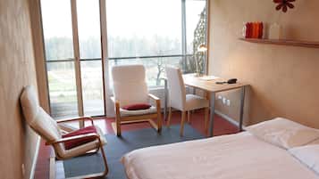 A hotel room with a bed, a desk, a chair, and a large window offering a view of the outdoors.