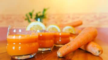 Three glasses of orange juice with lemon slices, a bunch of carrots, and a plant in the background.