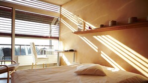 A bedroom with a bed, a chair, a small table, and a shelf with containers. - EcoHotel L'Aubier (Rochefort)