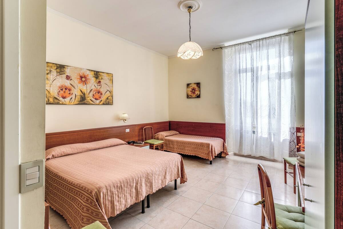 A hotel room with two beds, a wooden headboard, a single chair, a small table, and a painting on the wall.
