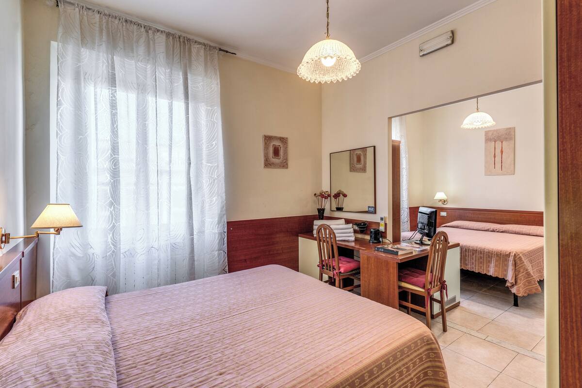 A hotel room with two beds, a desk with a chair, a lamp, and a mirror.