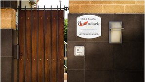 Uma entrada com portão e placa indicando 'ilmandorlo Bed & Breakfast', com informações de contato.