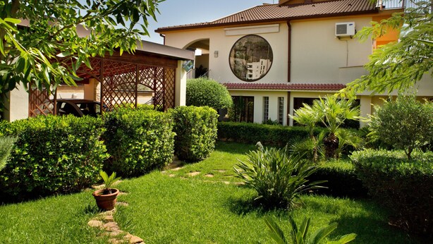 Uma casa com um jardim bem cuidado, uma janela circular e um pérgula.