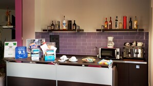 Uma área de recepção de hotel com balcão, diversos alimentos, uma máquina de café e uma seleção de garrafas de bebidas alcoólicas nas prateleiras.