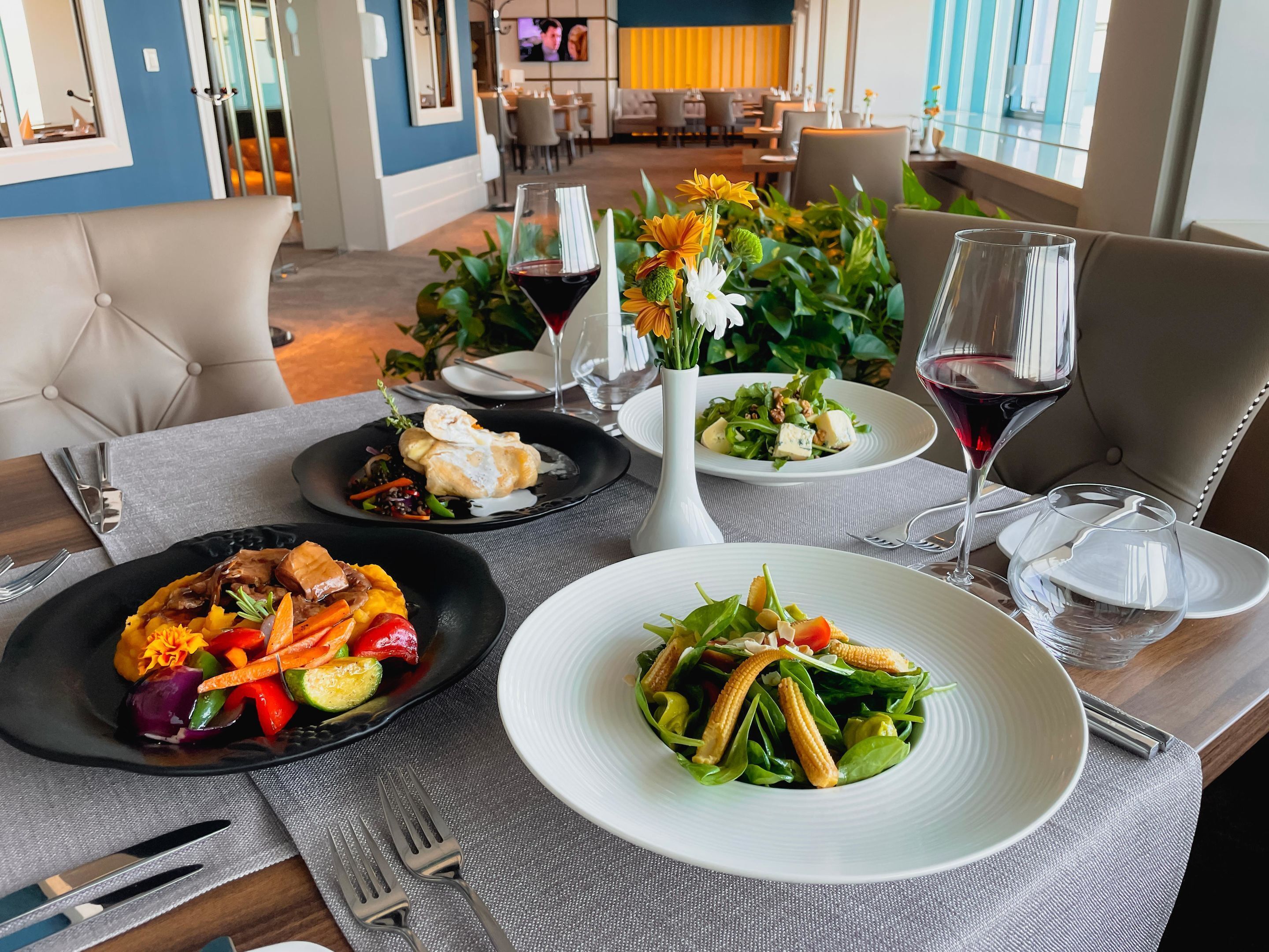A dining table with three plates of food, a vase with flowers, and wine glasses.